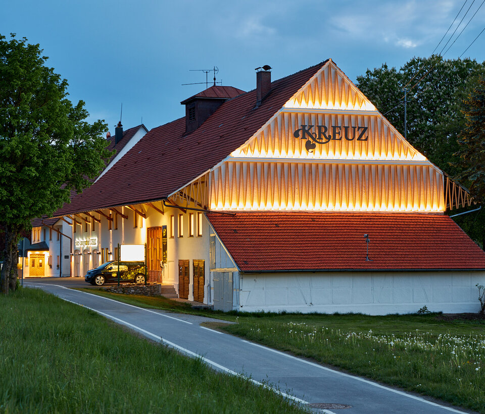 Außenansicht des Hotel-Landgasthof KREUZ bei Abendlicht Traditionelles Gebäude des Hotel-Landgasthof KREUZ mit rotem Dach und beleuchteter Fassade bei Dämmerung
