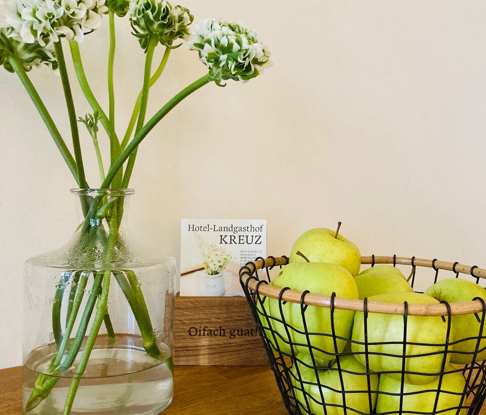 Detailaufnahme mit Dekoration im Hotelzimmer Vase mit weißen Blüten und grüne Deko auf Holztisch im Hotel-Landgasthof KREUZ
