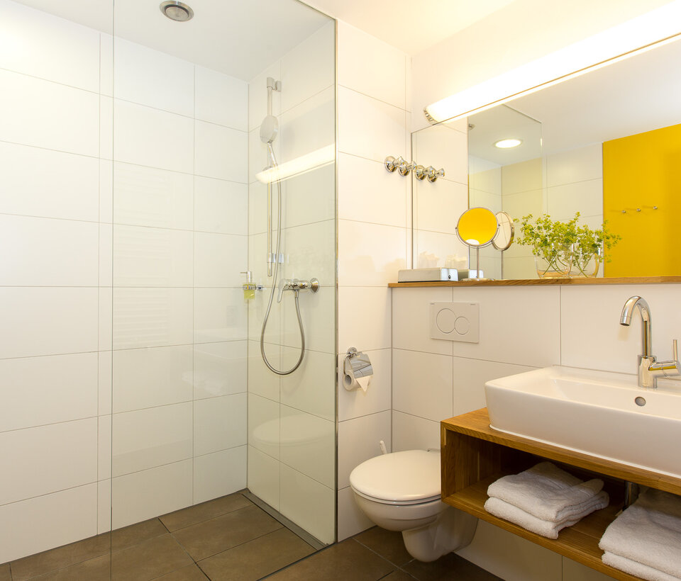 Badezimmer mit gelben Akzenten Modernes Bad mit Dusche, gelber Wandgestaltung und Handtüchern im Hotel-Landgasthof KREUZ