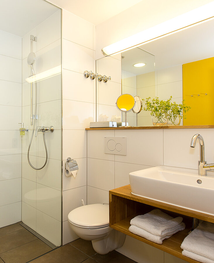 Badezimmer mit gelben Akzenten Modernes Bad mit Dusche, gelber Wandgestaltung und Handtüchern im Hotel-Landgasthof KREUZ